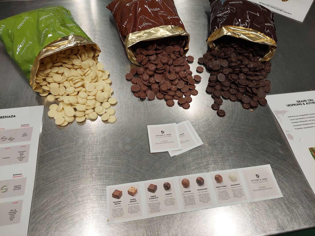 Open bags of white, milk and dark chocolate drops on a steel counter